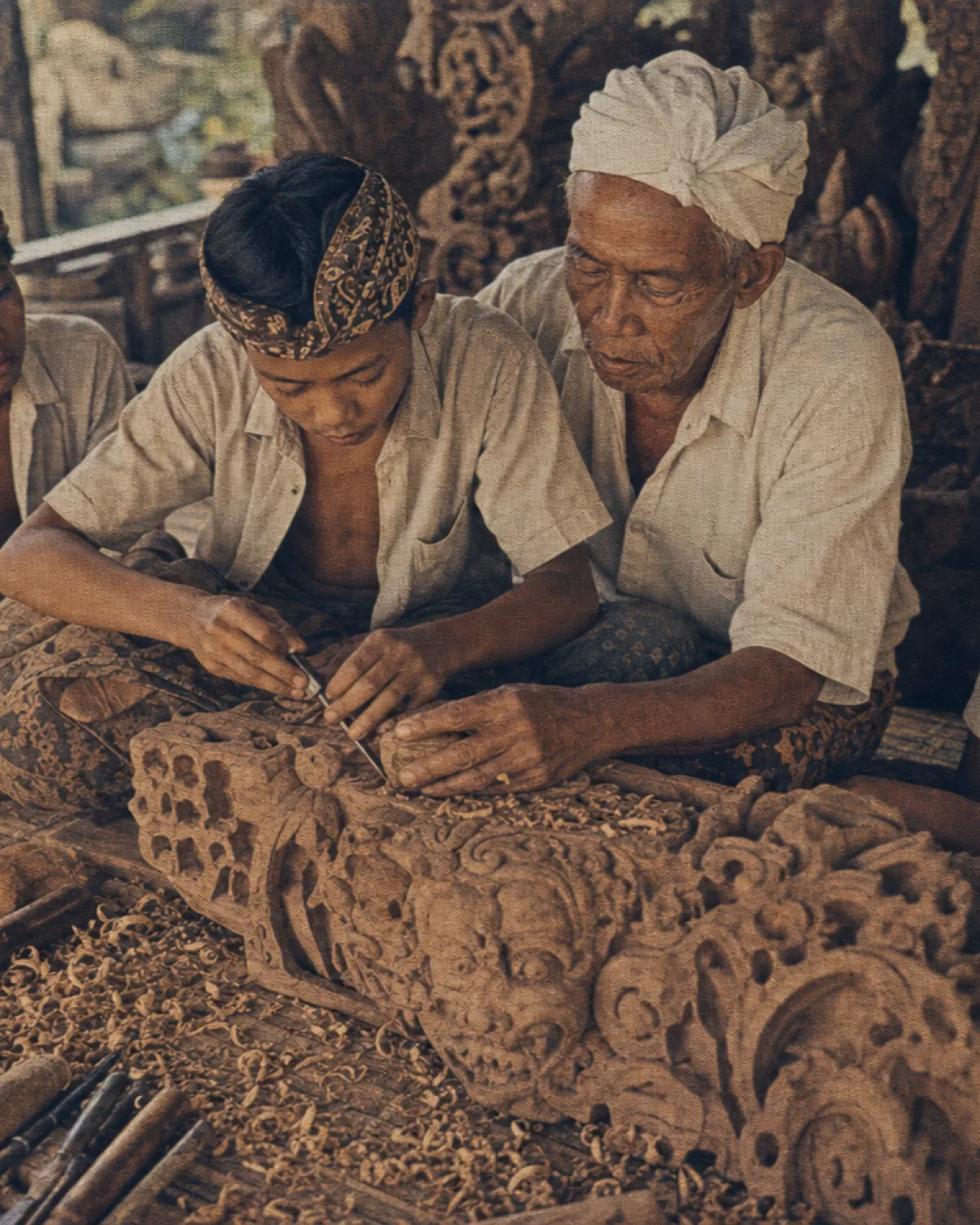 Elder Balinese woodcarver teaching young apprentices in a workshop, vintage archival print