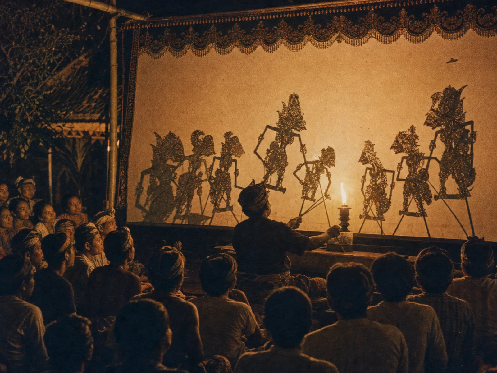 Wayang kulit shadow-puppet screen glowing at a night performance, vintage archival print