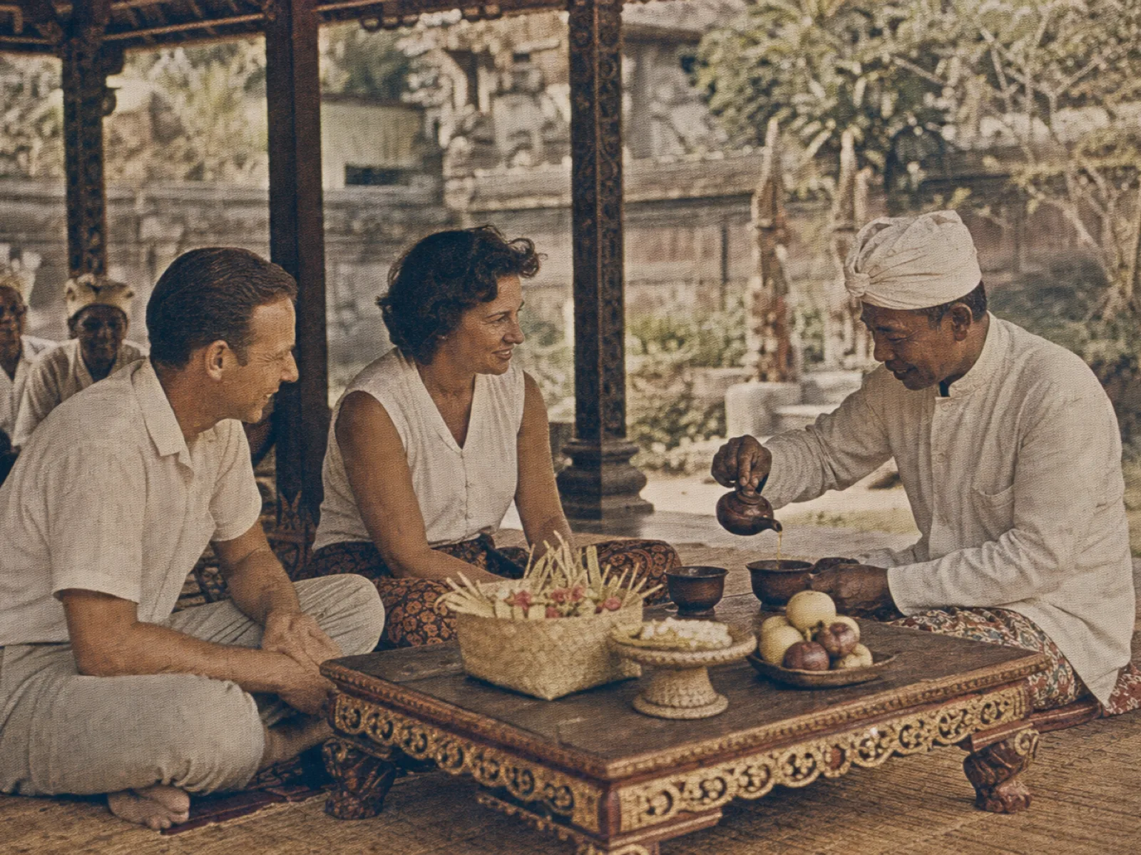 Village head sharing tea with visiting guests in a Balinese pavilion, vintage archival print