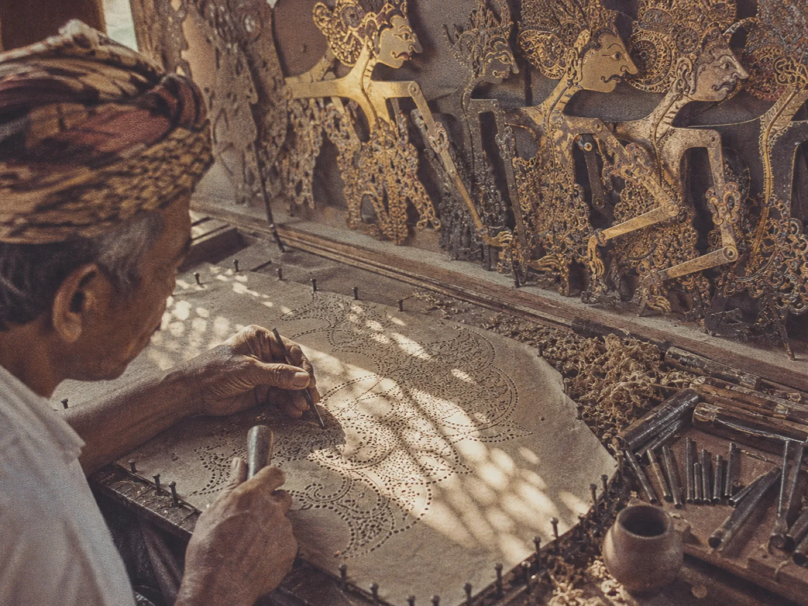 Hands carving perforations into a wayang kulit leather puppet, vintage archival print